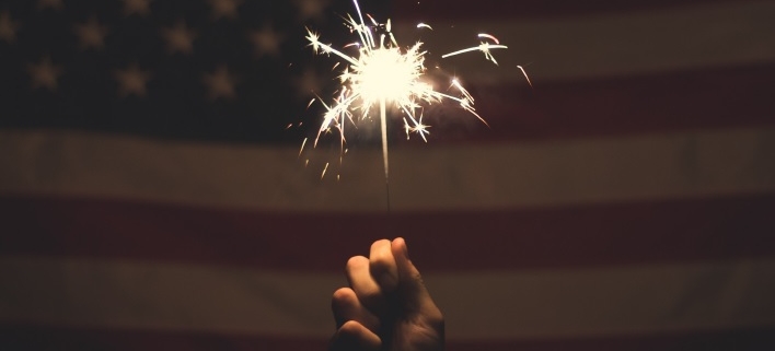 Hand holding sparkler in front of American flag