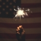 Hand holding sparkler in front of American flag